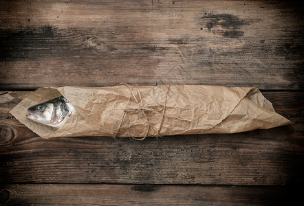 用棕色纸包裹的新鲜大海贝斯鱼与绳子木桌顶视角捆绑在一起图片