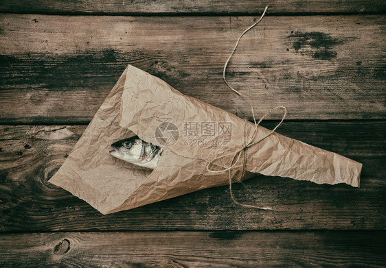 用棕色纸包裹的新鲜大海贝斯鱼与绳子木桌顶视角捆绑在一起图片