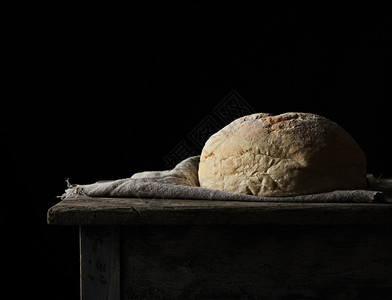 在毛巾上烤圆白小麦面包木制旧桌子黑色背景土制食品图片