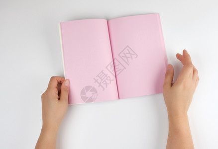 两只女手握着张开的笔记纸上面是白色背景的干净粉红色床单图片