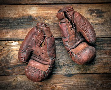 在破旧木板上戴着非常老旧的皮革棕色拳击手套图片