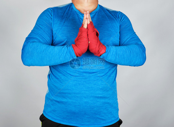 穿蓝制服的成年男子运动员身着祈祷姿势双手用红色运动绷带包起来胸前手掌结在一起图片