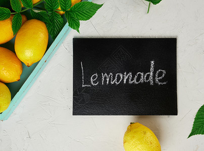 新鲜成熟的全黄色柠檬和黑色框架上面写着柠檬水是制作饮料的原料灰色背景图片