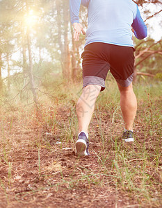 身穿蓝衣服和黑短裤的成年男子在阴险的森林中奔跑对抗明亮的太阳健康生活方式的概念和在新鲜空气中奔跑图片