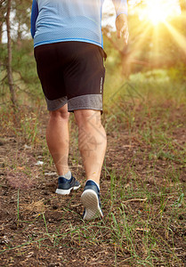 穿着蓝衣服和黑短裤的成年男子沿着迷幻的森林奔跑对抗明亮的太阳健康生活方式的概念和在新鲜空气中奔跑图片