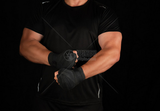 身穿黑色制服的成年人运动员站在一个肌肉紧张的架子上双手被黑色的纺织绷带深底包裹在黑色的纺织绷带中图片