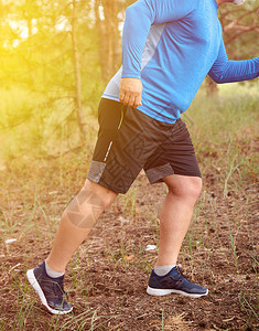 穿蓝制服运动鞋和黑短裤的成年男子运动健壮员在夏夜穿过树林中部外出运动和健康生活方式的概念图片