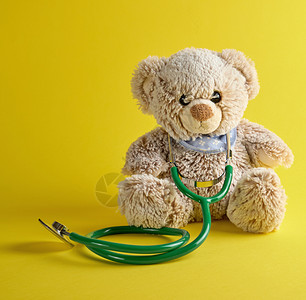 灰色泰迪熊和黄背景的绿医学听诊器儿童治疗概念背景