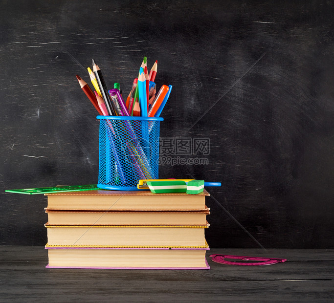 书和蓝色文具玻璃装有多色木铅笔和标尺空白黑粉笔板背景上的橡皮纸回到学校概念图片