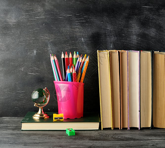 在空黑粉笔板背景的空黑粉笔板上用多色木铅笔蓝文具玻璃和一堆书蓝色文具回到学校概念图片