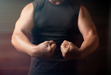 有运动身材的成年男子穿黑衣服的男子将肌肉塞在手臂上健美运动员展示了他的二头肌低键图片