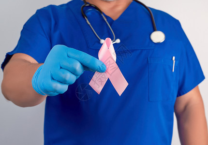 蓝制服医生和无菌乳胶手套的蓝制服医生和无菌乳胶手套佩带粉红色丝这是10月2日防治乳腺癌斗争的象征图片