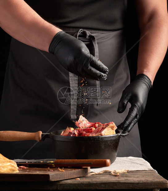 黑制服厨师和穿色制服的手套,在黑铁煎锅里做生鸡肉,饭图片