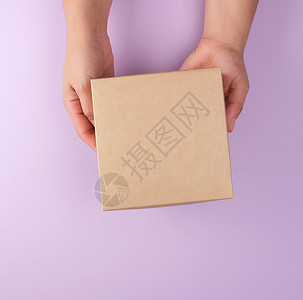 女孩在紫色背景上持有棕色的方盒子顶级观点赠送礼物的概念图片