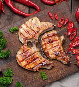 肋骨上的猪肉炸牛排躺在古老的棕褐木板上旁边是新鲜红辣椒图片
