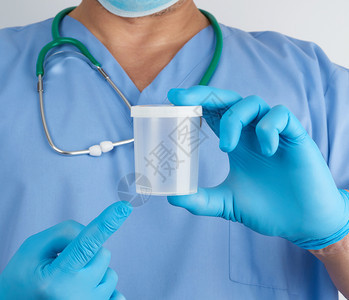 穿蓝色制服和乳胶手套的医生拿着一个空塑料容器用于取尿液样本并关闭图片