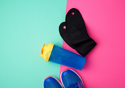 蓝色鞋带塑料水瓶和黑色手套的一对运动鞋彩色抽象背景顶视测试地点图片