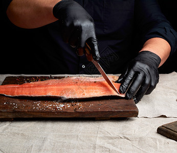 黑衣厨师和乳胶手套把新鲜的鲑鱼肉片切成碎黑钥匙图片