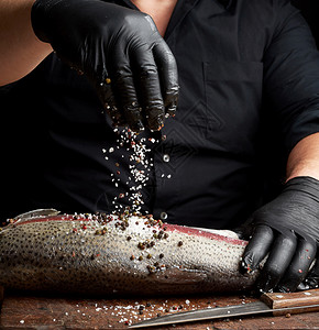 黑衬衫主厨和乳胶手套准备木制切板上的鲑鱼片配香料和盐低键图片