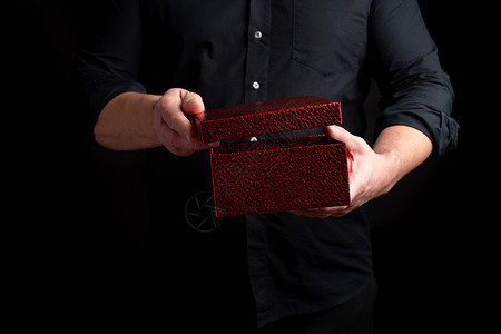 穿黑衬衫的成人男子拿着一个纸板红礼盒打开盖子黑暗背景图片