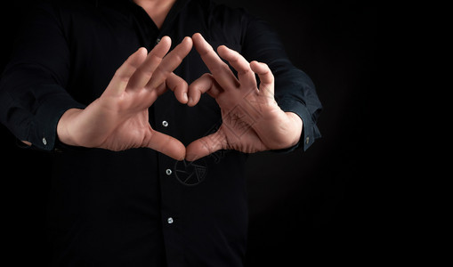 穿黑衬衫的成人男子举起双手在黑暗背景爱与和平的概念下用心示背景图片