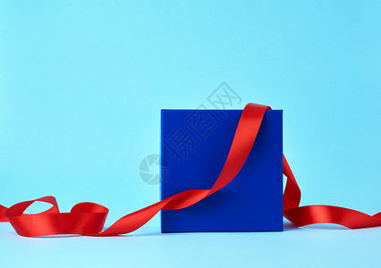 蓝纸箱用于赠品和蓝色背景的扭曲丝绸红色带图片
