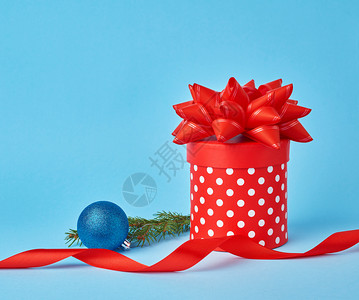 红色圆点圆形的红色纸板箱白色圆点带蝴蝶结云杉枝蓝色背景上有一个闪亮的蓝色球圣诞节的背景背景