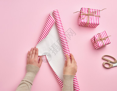 两只女手展开一卷包装纸紧靠两件礼物粉红背景准备惊喜图片