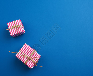 两件包裹在蓝色背景顶视图复制空间的粉红色条纹纸上的礼物图片