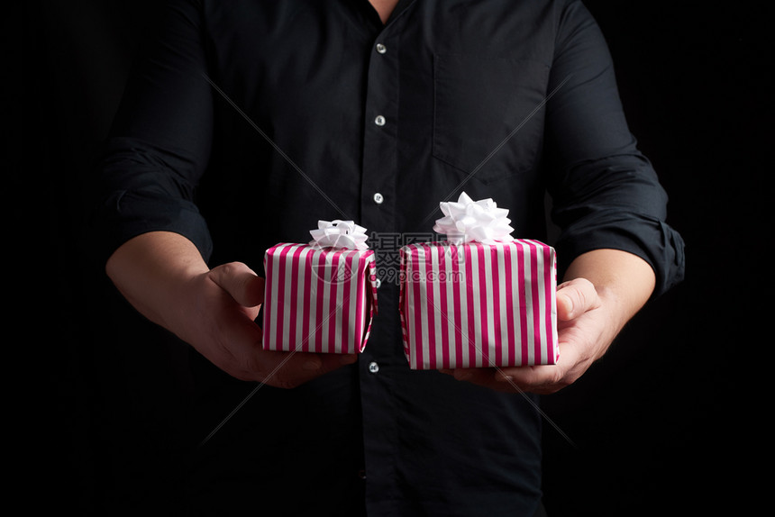 身穿黑衬衫的成人男子手上握着一堆纸包装的礼物节日问候的概念低调钥匙图片