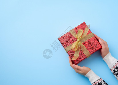 女手握着一个红色盒子绑着金丝带祝贺和礼物的概念顶视蓝底图片