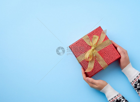 女手握着一个红色盒子绑着金丝带祝贺和礼物的概念顶视蓝底图片