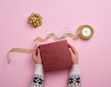 女手握红盒和金丝带祝贺礼物的概念顶视粉红色背景图片