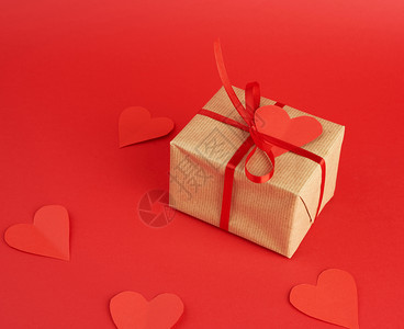 用棕色工艺纸包着礼物的方形盒子在红色的背景上系上一条薄薄的丝绸红丝带空纸心形的礼物图片