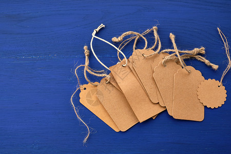 Kraft纸上空的棕色标签堆叠上面有用于衣服和其他途的绳索放在蓝色木制背景上设计元素图片