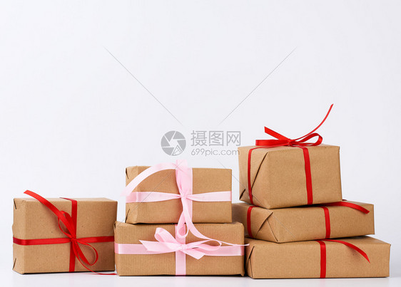 包装在着棕色Kraft纸和白色背景上带丝绑在白色背景上的盒子中一叠礼品图片