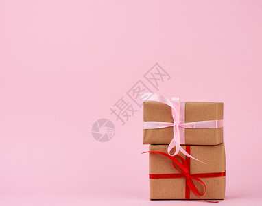 包装在着棕色克拉夫纸的盒子中并用粉红背景的丝带捆绑在粉红色背景上图片