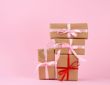 装在盒子里的礼物堆包在着棕色克拉夫纸的盒子里绑在粉红色背景的丝带上图片