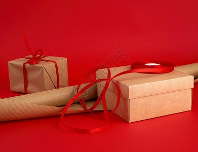 包装用的棕色纸卷红丝带和背景的棕色Kraft纸包装礼物图片