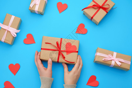 女手握着一个包棕色克拉夫纸的盒子并绑上蓝色背景的丝带纸红色心情人节的背景图片