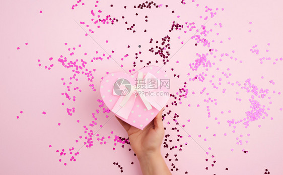 女手握着粉红纸板盒在背景上鞠躬面色多彩的条为假日赠送礼物的概念图片