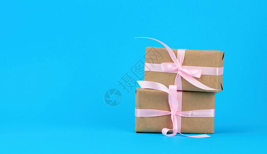 包在着棕色Kraft纸的盒装礼物中并用蓝色背景的粉丝带绑在蓝背景上图片