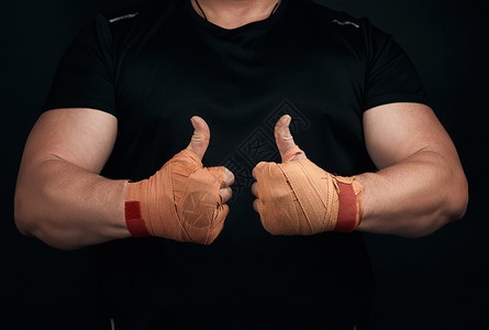 身穿黑色制服的肌肉运动员显示一个相似的符号有两只手用橙色纺织运动绷带包裹的手掌黑色背景图片