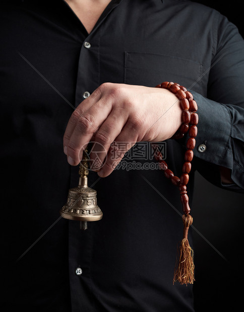 身穿黑衬衫的成年男子拿着铜藏仪式钟图片