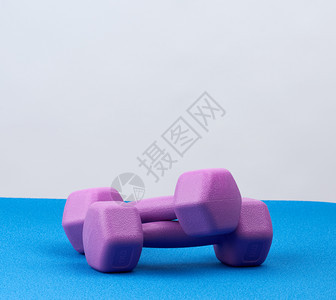 蓝色地毯上运动用的紫色塑料哑铃白背景健身训练康的生活方式图片