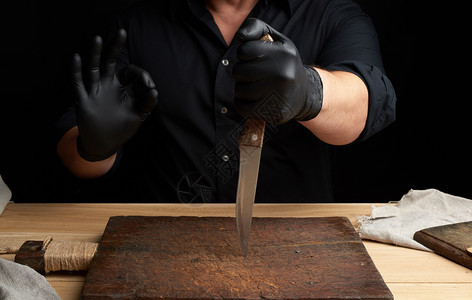 黑衬衫主厨和乳胶手套拿着一把大刀切肉右手显示好的符号低键图片
