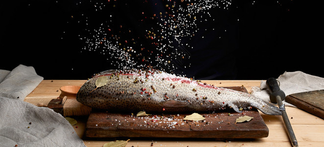 木板上的无头鲑鱼片洒满大块白盐和胡椒烹饪鱼的过程低键图片