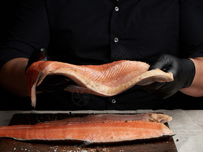 黑衬衫厨师和乳胶手套餐桌上有一大片鲑鱼烹饪过程挤压图片
