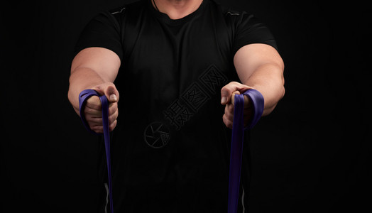 身穿黑衣肌肉的运动员正在用低密钥紫色橡胶进行体操图片
