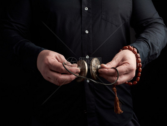身着黑衣服的成人男子手里握着一对用皮绳宗教仪式用物冥想和替代药低键的铜制Karatal图片